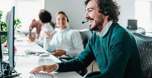 Smiling IT helpdesk agent with a headset at his computer